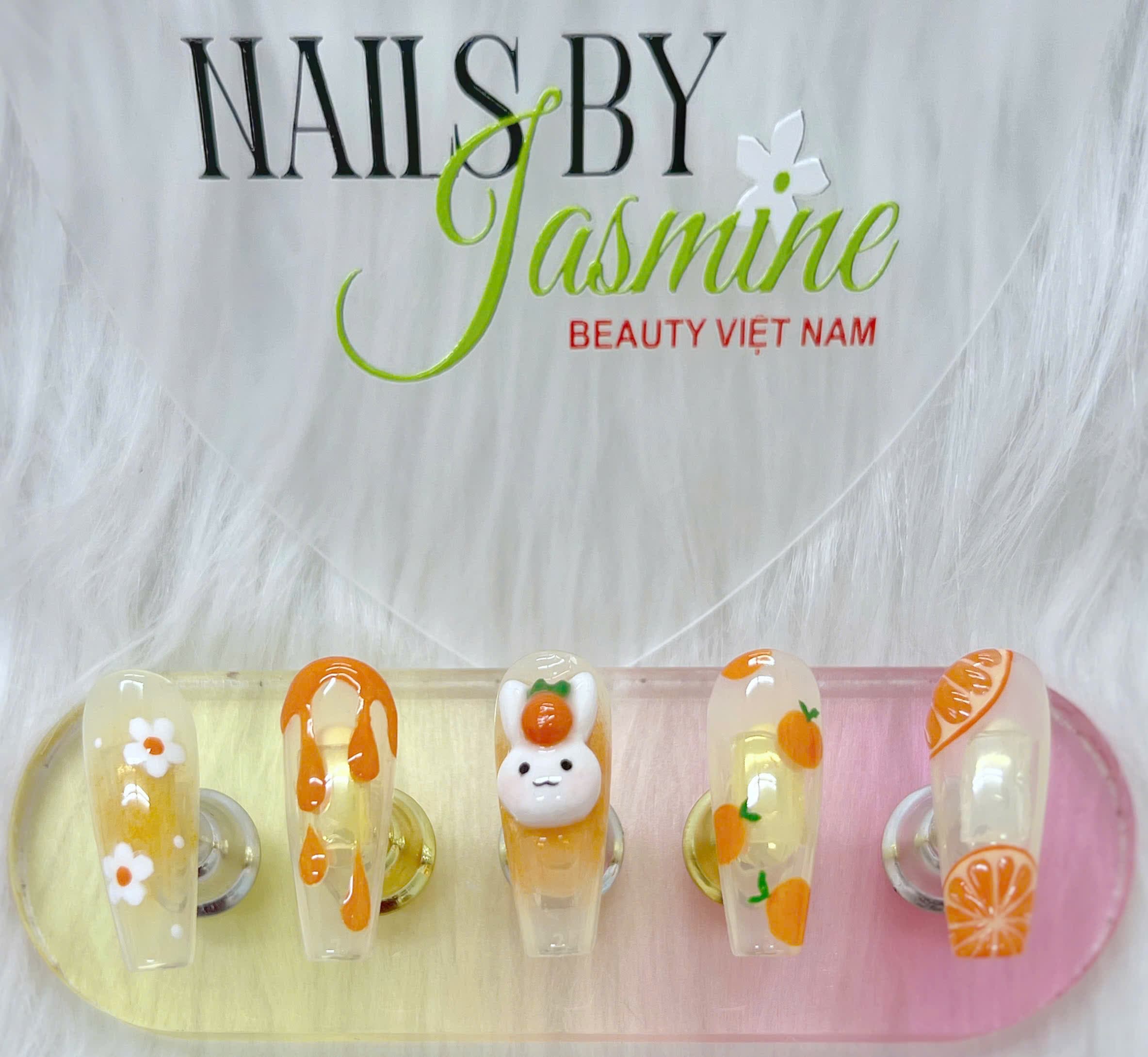 Bộ móng cam hoạt hình với họa tiết thỏ trắng, lát cam và hoa baby trên nền gel vàng nhạt, mang phong cách dễ thương và tươi mát do học viên Jasmine thực hiện
