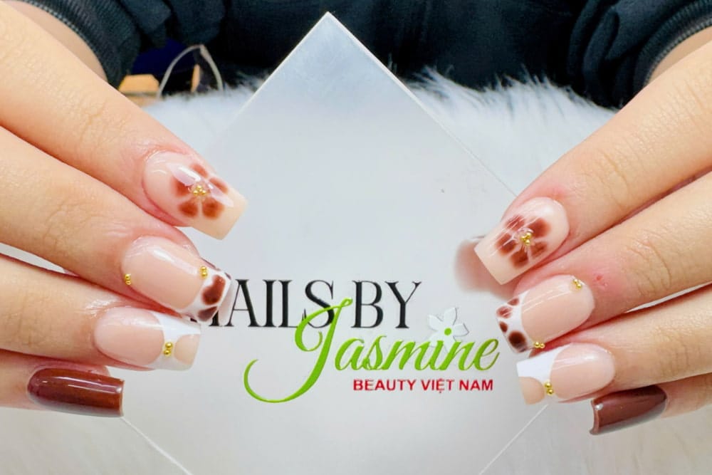 Mẫu gel hoa loang đơn giản cho người học nail – kết hợp sơn nền tự nhiên, kỹ thuật loang gel vẽ hoa nâu, viền French trắng và đính charm vàng.